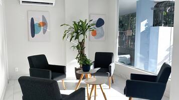 Um espaço de escritório moderno com uma janela grande, duas cadeiras pretas, uma pequena mesa e uma planta em vaso.