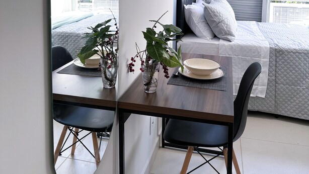 A modern room with a bed, a dining table with chairs, and a large mirror reflecting the room. - CoVívere - RJ (Rio de Janeiro)