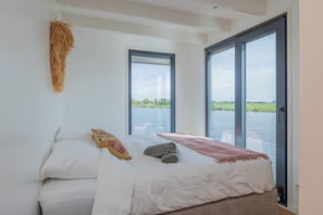 A bedroom with a bed, a window, and a view of a body of water.