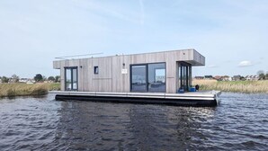 Uma casa moderna flutuante com grandes janelas, telhado plano e um cais.