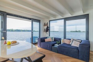 A modern living room with a glass table, two sofas, and a view of a body of water. - Luxury Houseboat `Surla CopesClub` & Free Dinghy (Warmond)