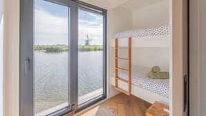 Quarto com beliche, vista para um corpo d'água e um moinho, e piso de madeira.