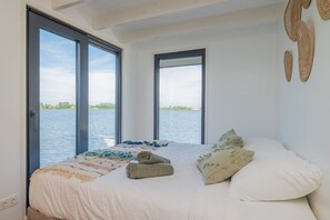 A bedroom with a large bed, a view of water, and a door leading to an outdoor area.