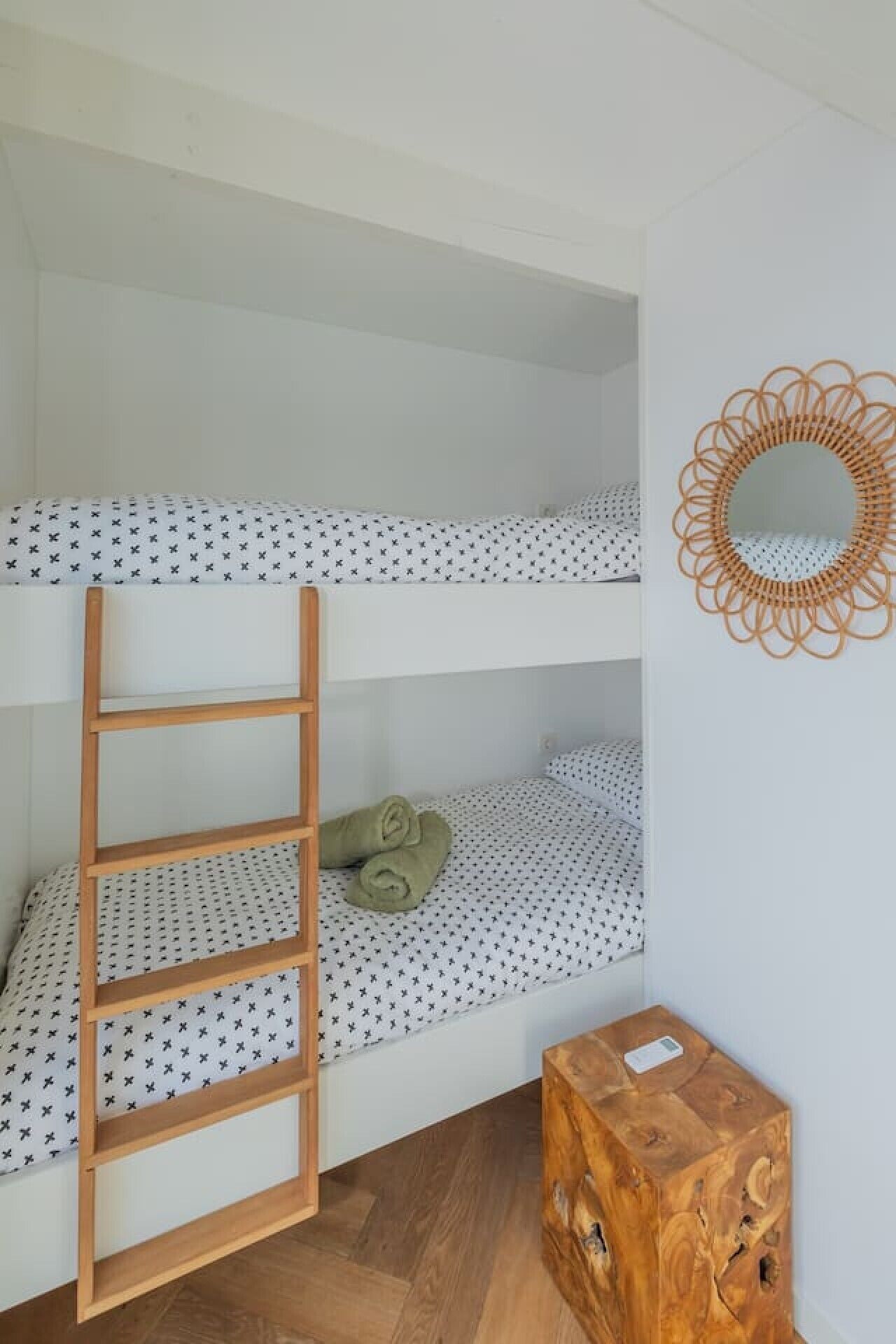 Un lit superposé avec une échelle, un matelas à motifs et une petite boîte en bois.