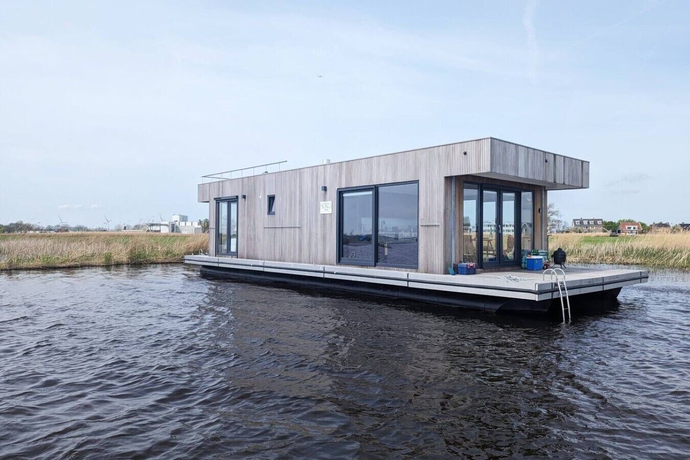 Une maison flottante moderne dotée d’un toit plat, de grandes fenêtres et d’une petite terrasse.