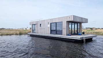 Une maison flottante moderne dotée d’un toit plat, de grandes fenêtres et d’une petite terrasse.