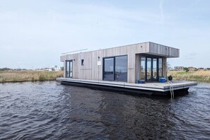 A modern floating house with a flat roof, large windows, and a small deck.