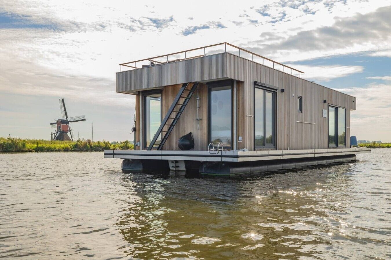 Une maison flottante moderne dotée d’un toit plat, de grandes fenêtres et d’une terrasse en bois.