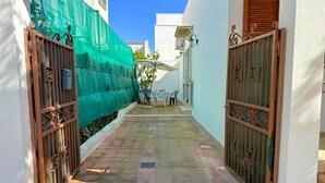 Un callejón estrecho con una cerca verde a un lado y una entrada protegida por una puerta a otro.