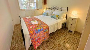 Una cama bien hecha con un edredón colorido, una lámpara de noche y un suelo estampado.