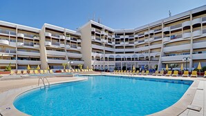 Une grande piscine entourée d’un immeuble à plusieurs étages, doté de balcons et de chaises longues.