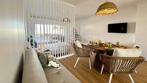 A modern living room with a sofa, dining table, wicker chairs, and a TV mounted on the wall. - VILAMOURA MARINA CHARMING WITH POOL by HOMING (Vilamoura)