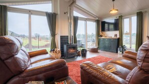 Een ruime woonkamer met lederen banken, een open haard en een grote televisie.