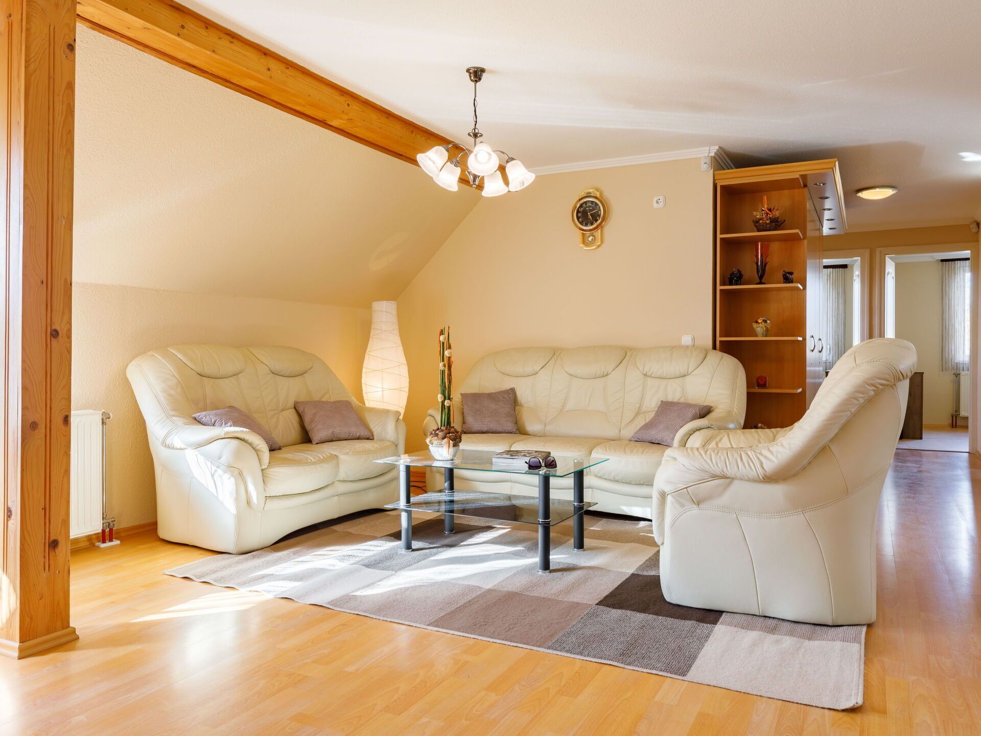 Ein geräumiges Wohnzimmer mit hoher Decke, einem Holzbalken, einem Glastisch, zwei Sofas und einer Stehlampe.
