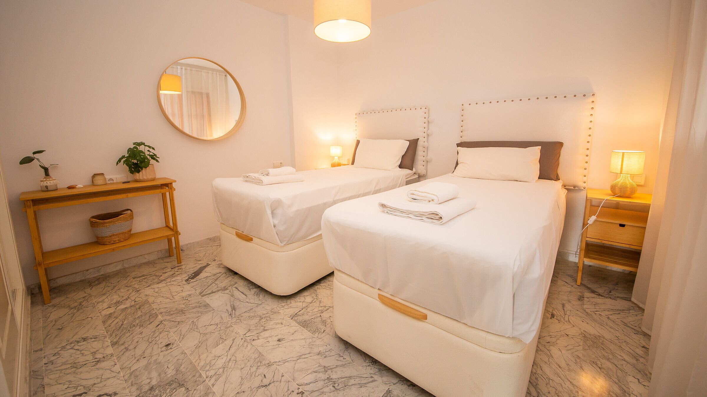 A hotel room with two beds, a bedside table, a mirror, and a lamp.