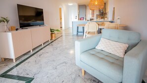 Ein modernes Wohnzimmer mit Flachbildfernseher, einer Couch, einem Essbereich und einer Küche im Hintergrund.