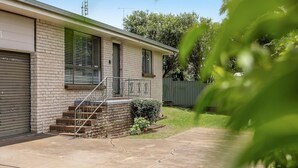 Uma casa térrea com fachada de tijolos, varanda frontal com degraus e um pequeno jardim.