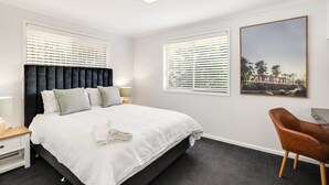 Quarto com cama, mesas de cabeceira, uma cadeira e um quadro grande na parede.