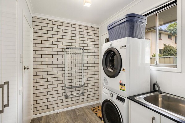 A laundry room with a brick wall, a washing machine, a dryer, and a sink.
