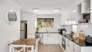 Uma cozinha moderna com armários brancos, uma mesa de jantar de madeira e um forno embutido.
