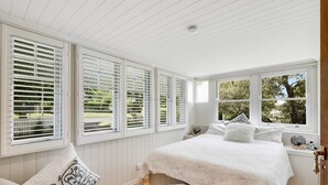 Une chambre à coucher avec un grand lit, des murs blancs et de nombreuses fenêtres équipées de stores.