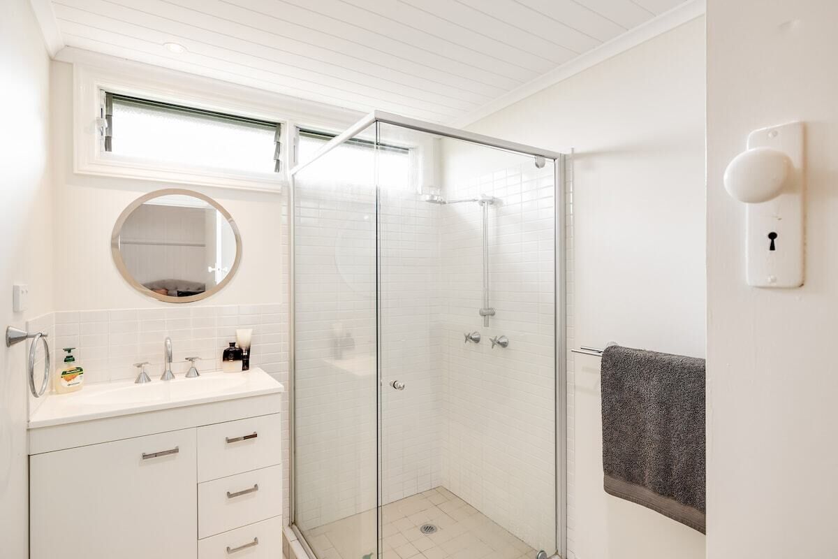 A bathroom with a glass-enclosed shower, a sink with a mirror above it, and a towel rack on the wall.