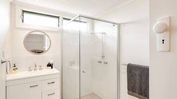 A bathroom with a glass-enclosed shower, a sink with a mirror above it, and a towel rack on the wall.
