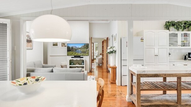 Une cuisine moderne avec des meubles blancs, une table à manger en bois et un grand luminaire suspendu blanc.