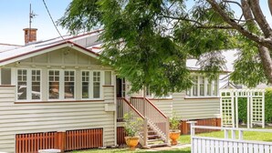 Une maison à deux étages, avec une façade blanche, une terrasse en bois et un escalier menant à l’étage supérieur.