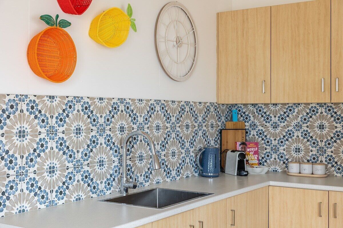 Una cocina con salpicadero decorativo, armarios de madera, un fregadero y un mural con frutas.