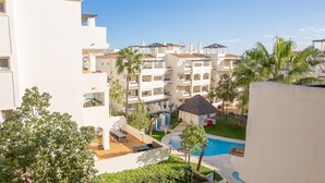 A resort with multiple white buildings, a swimming pool, and palm trees. - Residencial Duquesa 12 39 2b (Manilva)