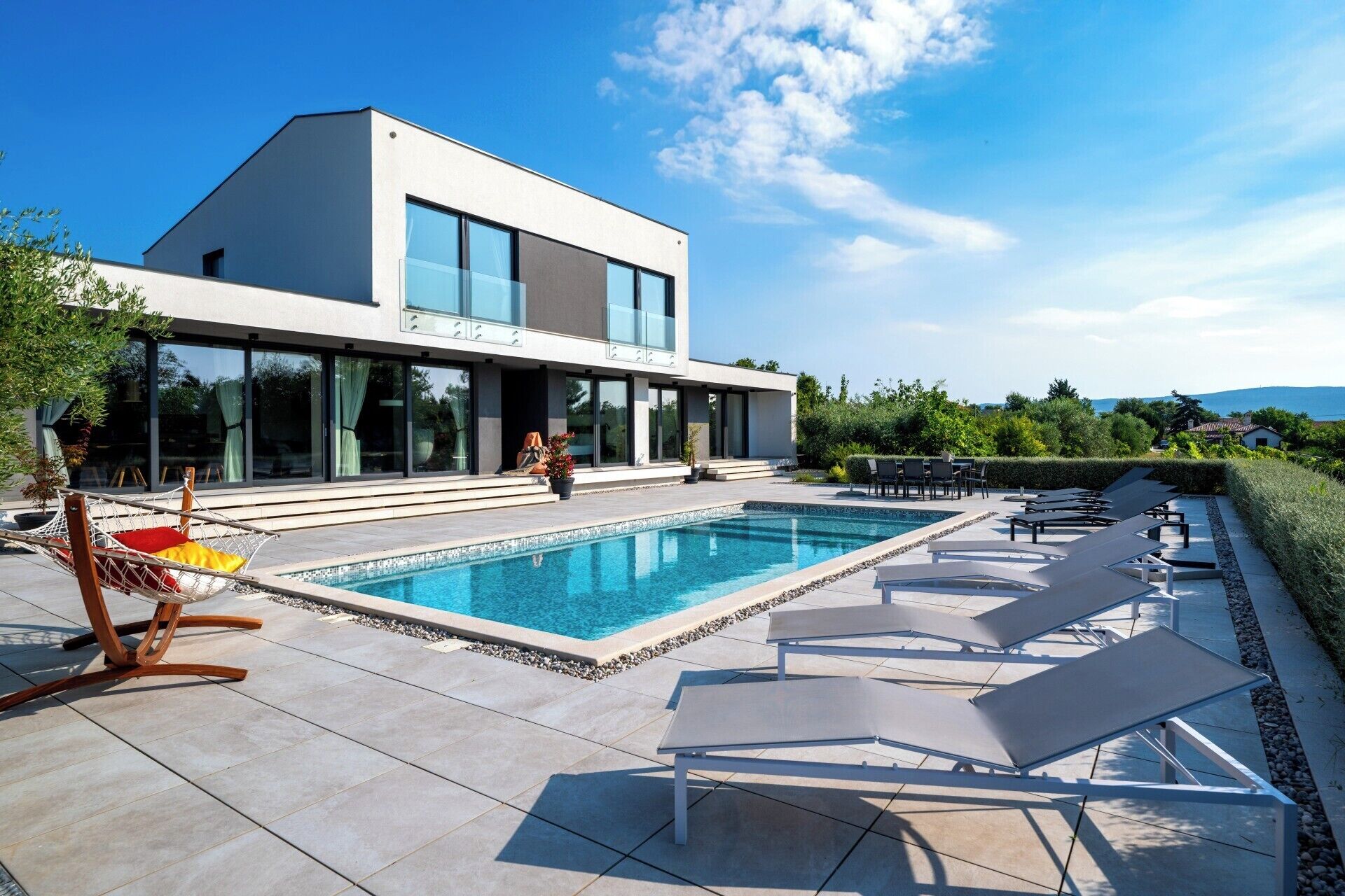 A modern house with a swimming pool, lounge chairs, and a hammock.