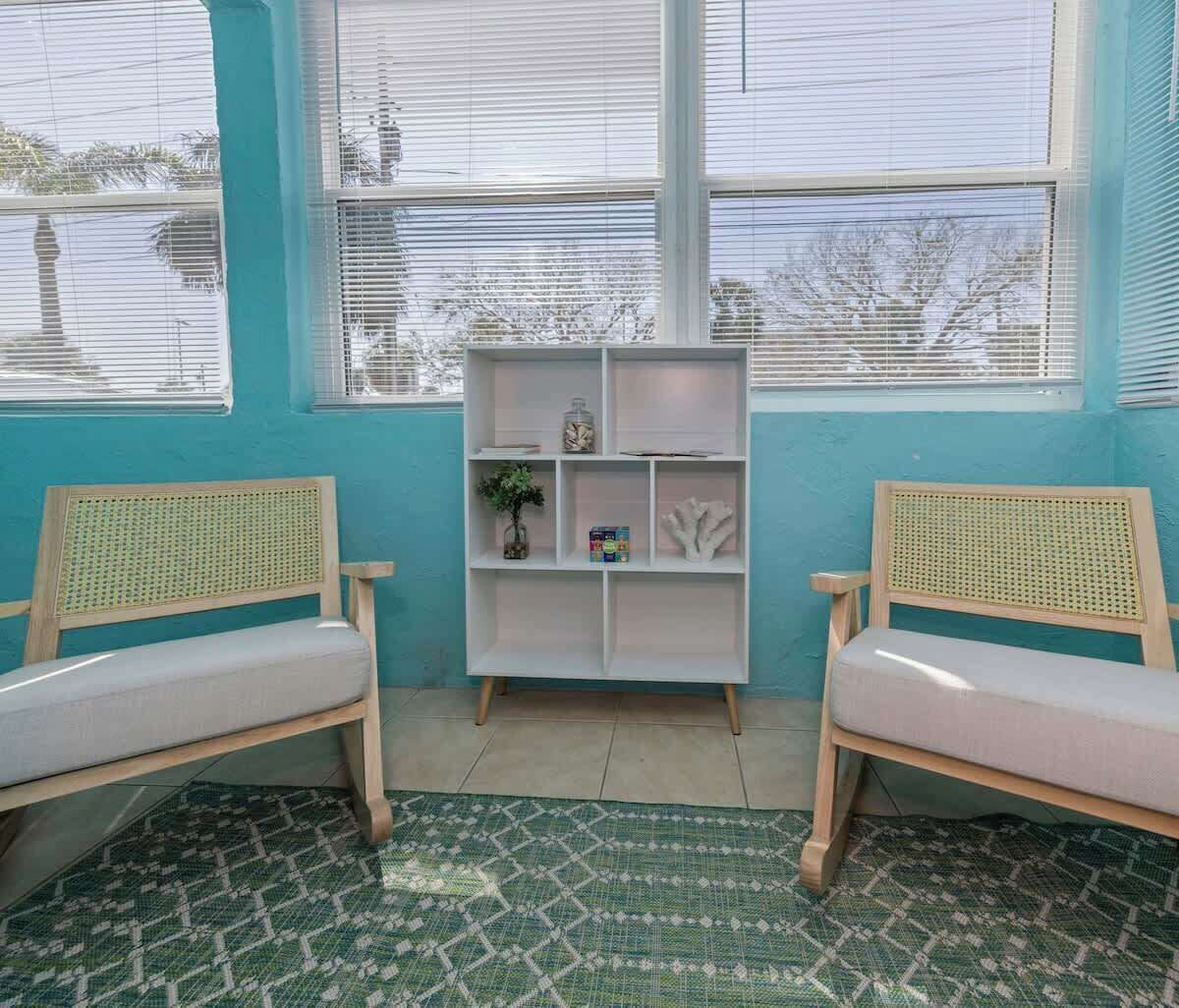 A room with two wooden chairs, a white shelving unit, and a patterned rug.