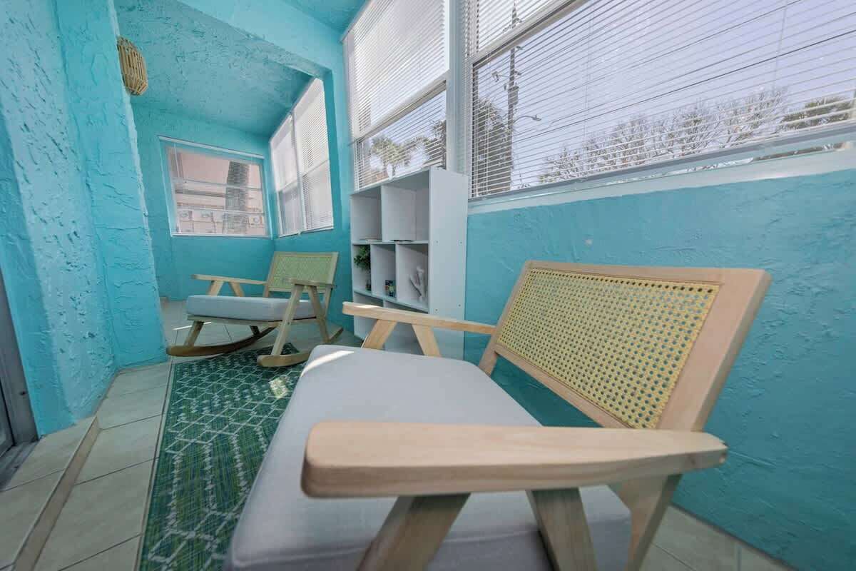 A room with teal walls, a wooden bench, a rocking chair, and a window with blinds.