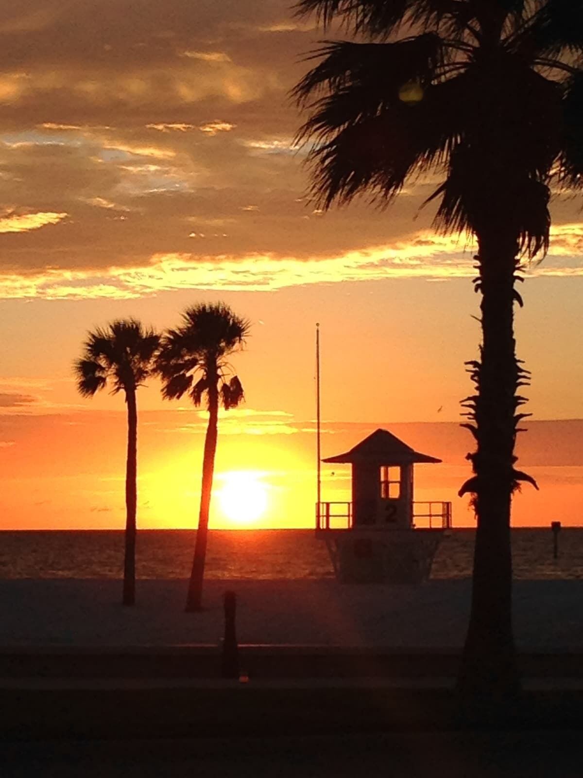 A beach scene with palm trees and a lifeguard tower during sunset.