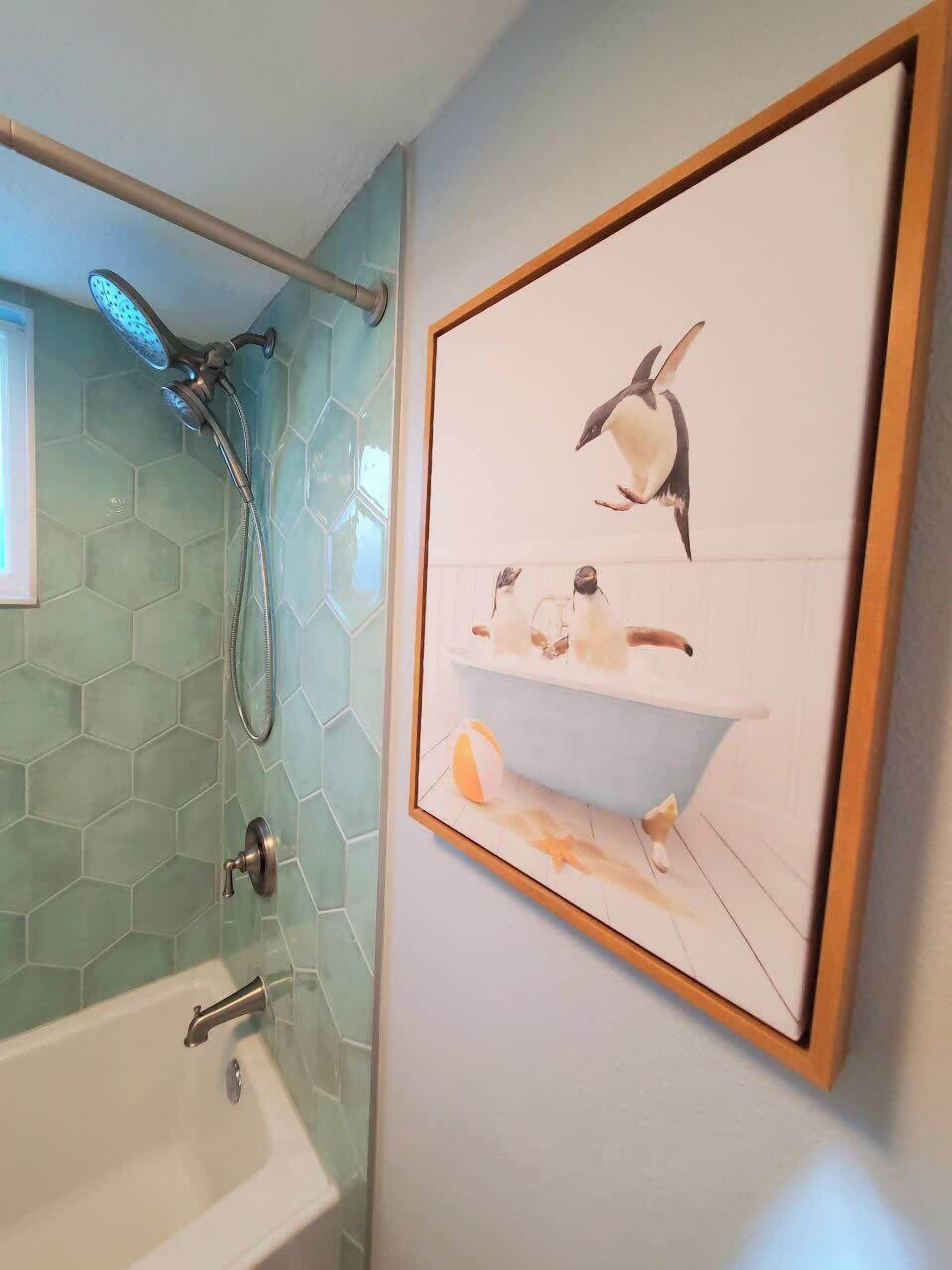 Ein Badezimmer mit Dusche, Badewanne und einem gerahmten Bild von Pinguinen an der Wand.