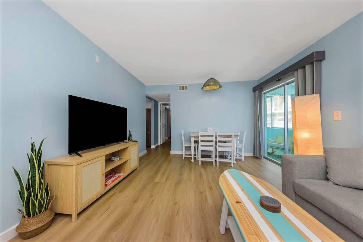A living room with a flat-screen TV, wooden entertainment unit, a bench, a dining table with chairs, and a sofa.