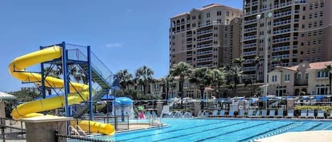 Una piscina con tobogán de agua, sillas de descanso y un edificio de hotel alto al fondo.