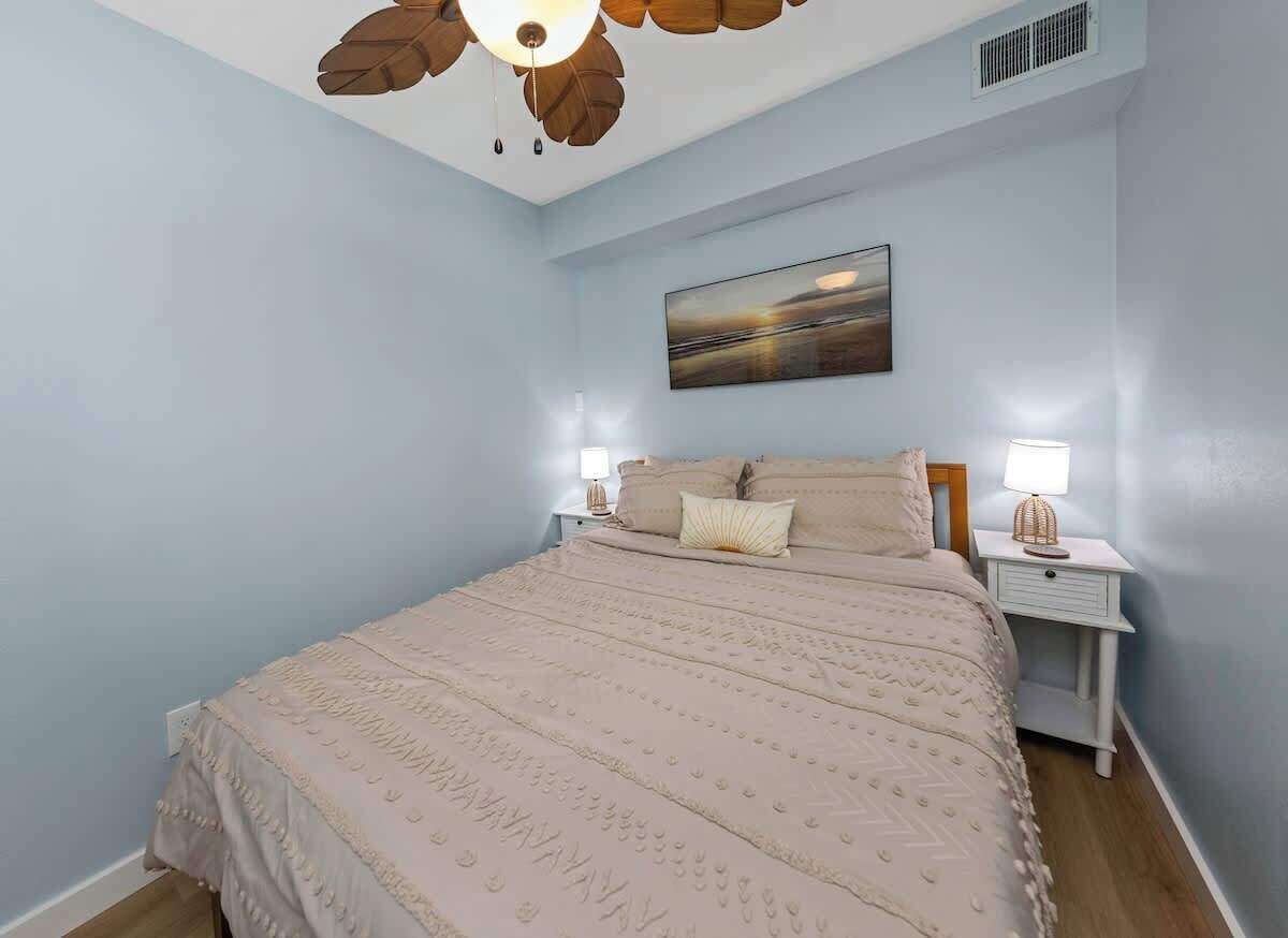 A bedroom with a bed, nightstands, a ceiling fan, and a painting on the wall.