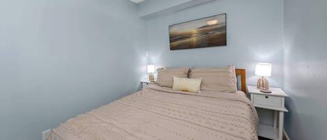 A bedroom with a bed, nightstands, a ceiling fan, and a painting on the wall.