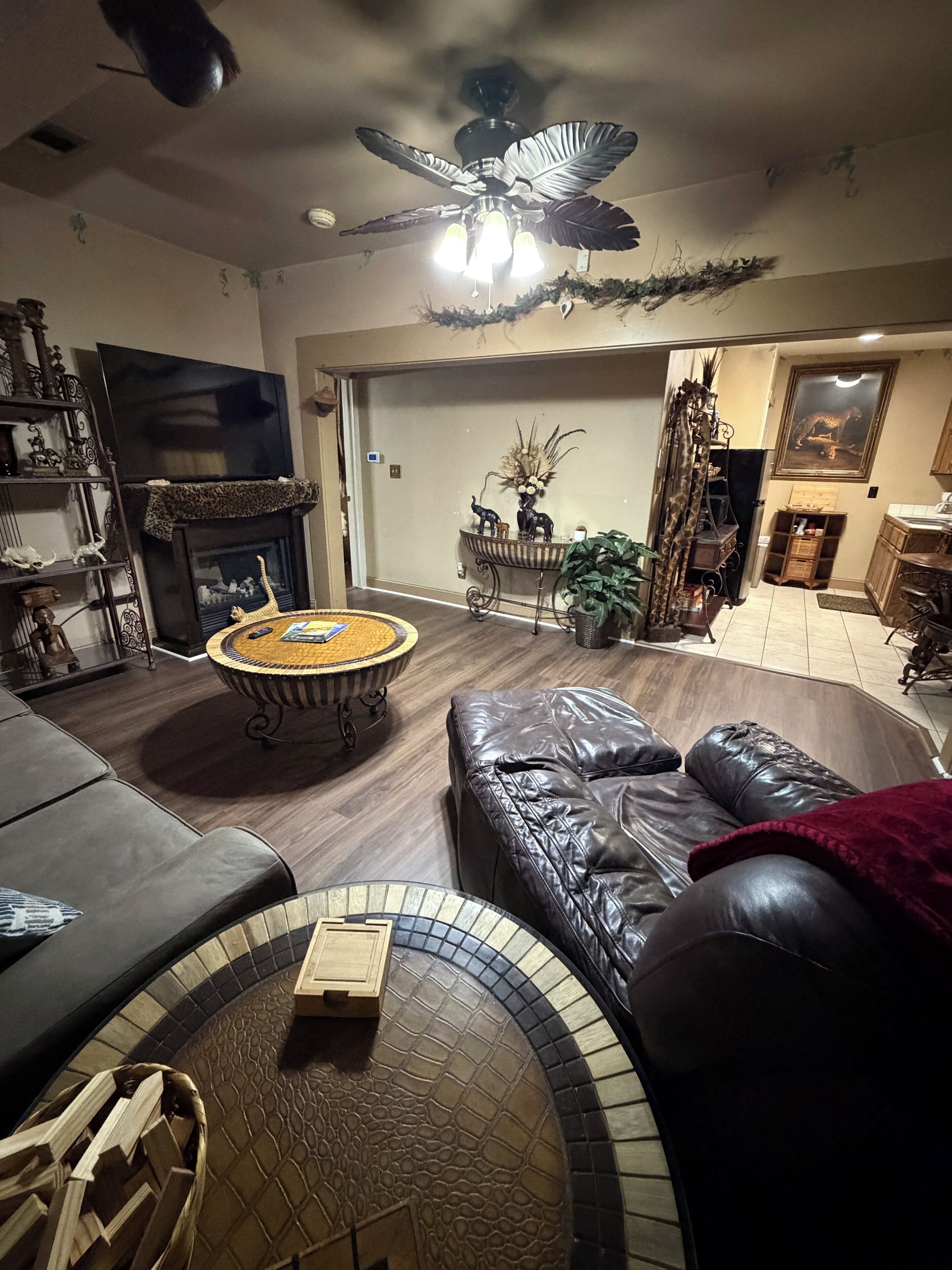 A living room with a fireplace, leather sofa, and a ceiling fan.