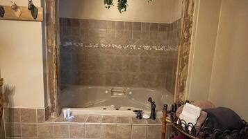 A bathroom with a bathtub, a wooden bench with towels, and a hanging plant.