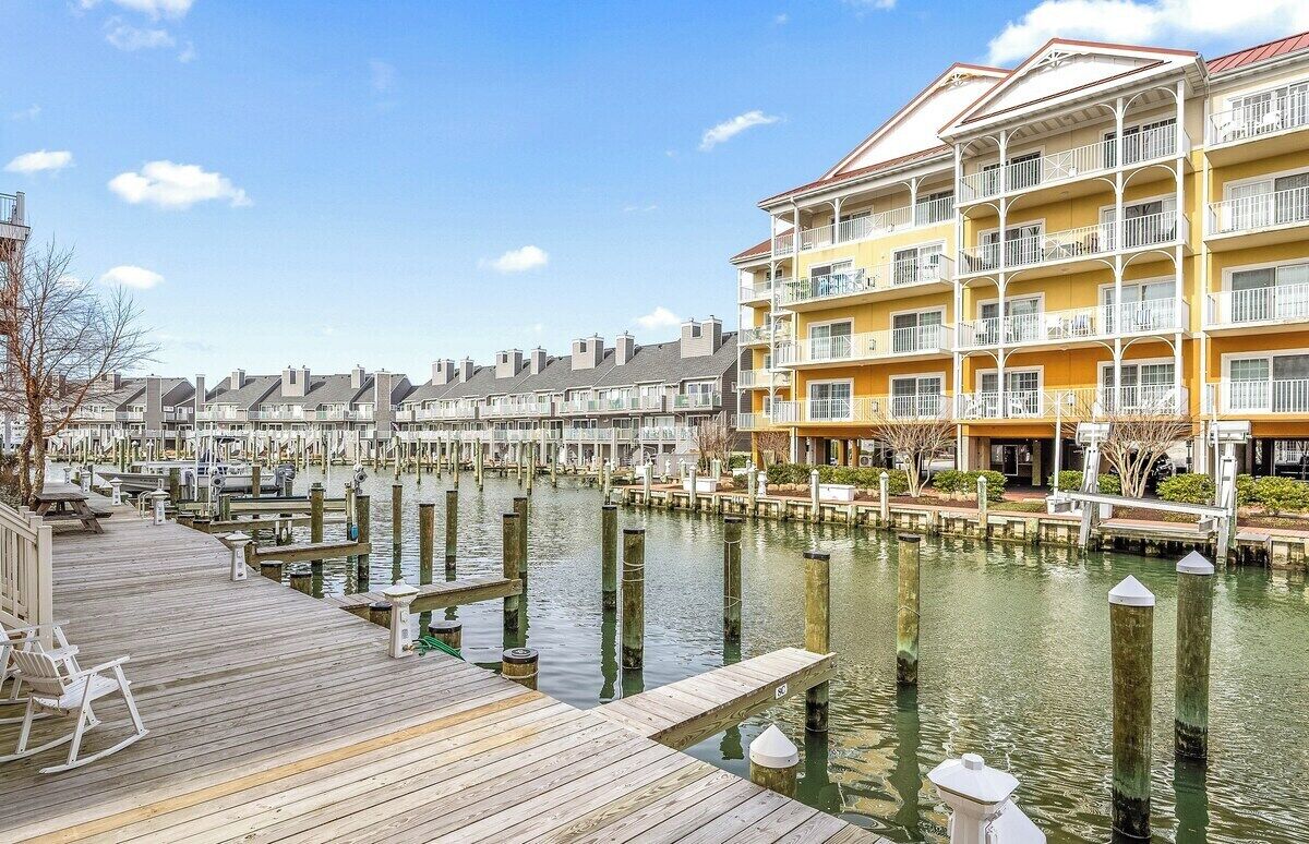 Un hotel frente al agua con varios balcones, una terraza de madera y un puerto deportivo.