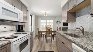 A kitchen with white appliances, granite countertops, and a dining area with wooden chairs. - Canalfront 2 Bedroom-Sleeps 6-Laundry-WiFi (Ocean City)