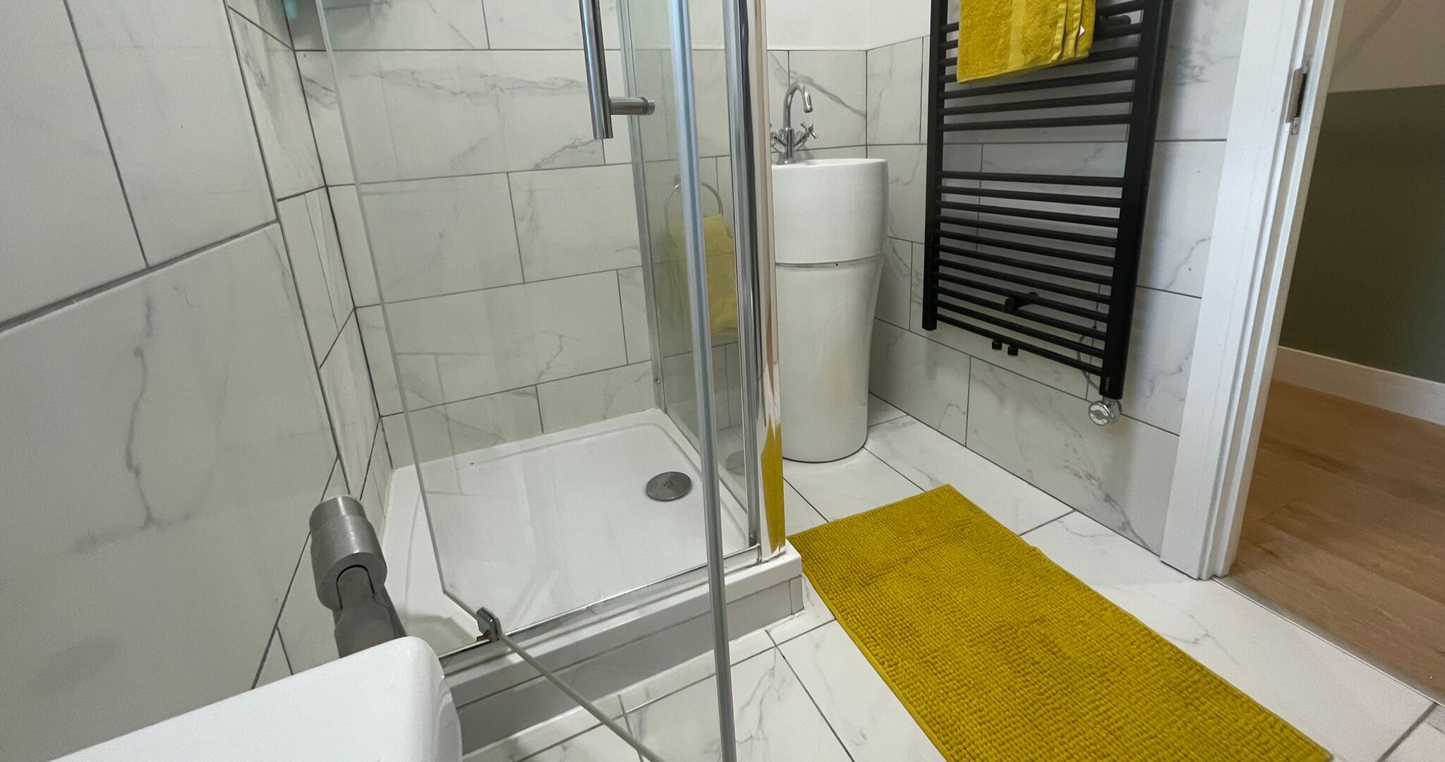 A modern bathroom with a glass shower enclosure, a white sink, and a black towel rack.