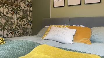 Una cama con un cabecero estampado, una manta amarilla y almohadas con detalles bordados.