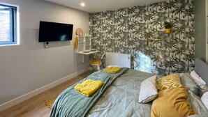 Quarto com cama, televisão na parede, radiador e estante com objetos.