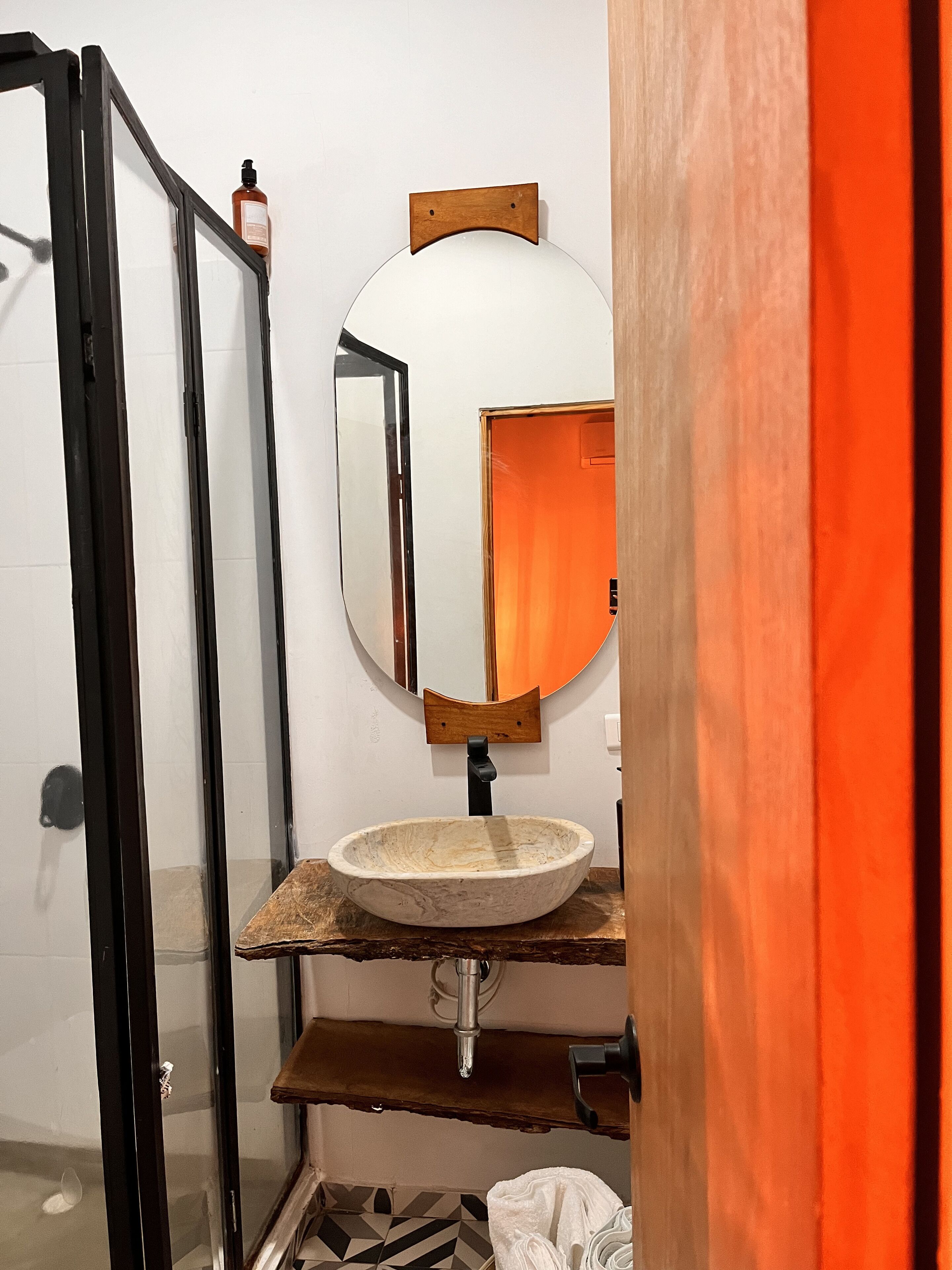 A bathroom with a wooden vanity, a round mirror, and a glass shower enclosure.