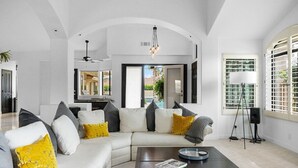 A modern living room with a sectional sofa, a coffee table, and a view of the outdoors. - Whispering Wells - Private Pool (Indian Wells)