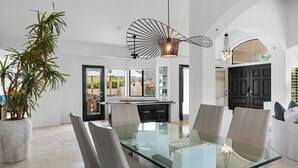 A modern dining area with a glass table, cushioned chairs, and a potted plant. - Whispering Wells - Private Pool (Indian Wells)